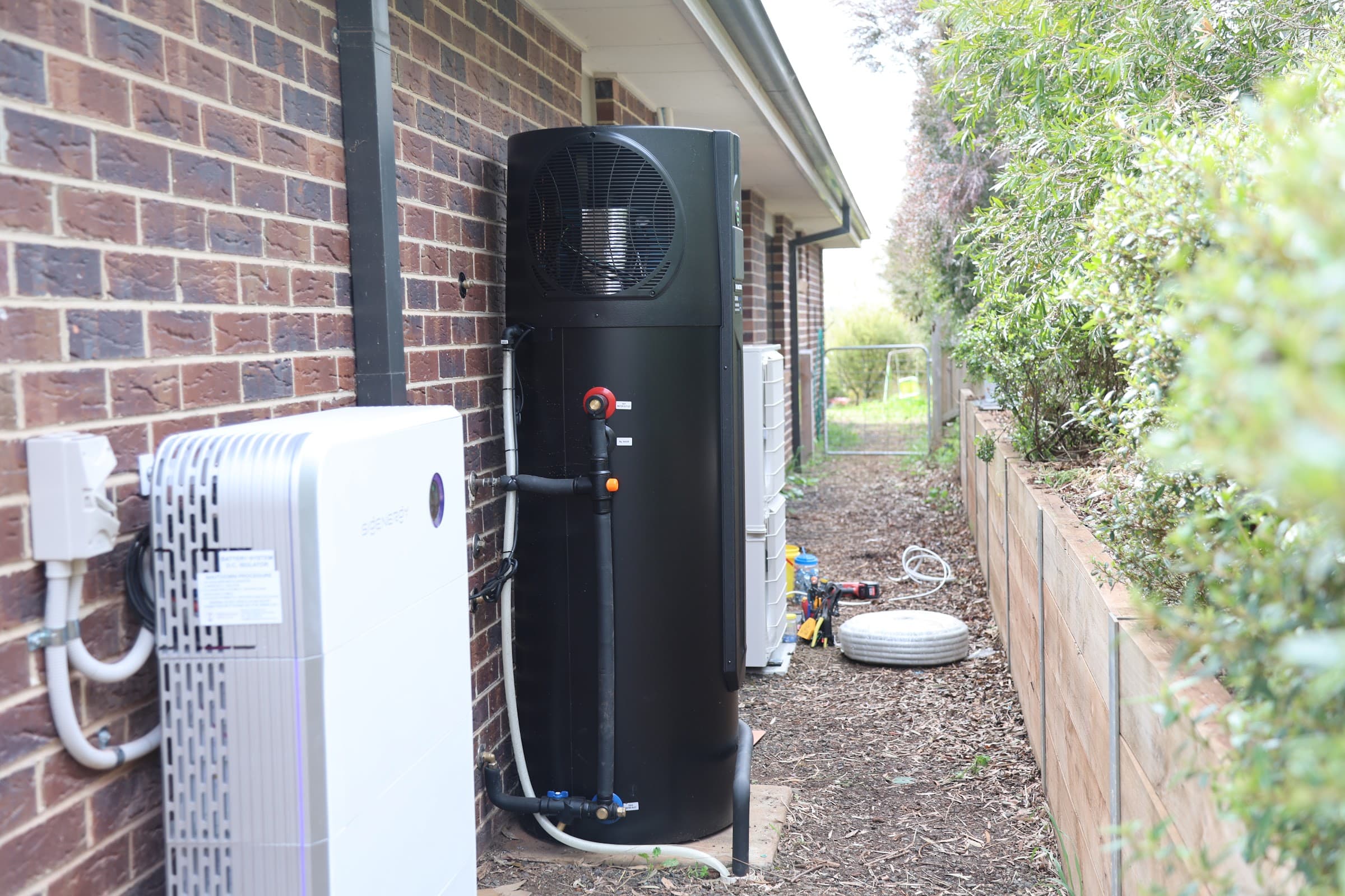 A fully electrified home: heat-pump hot water, battery and reverse-cycle condenser lined up along the wall