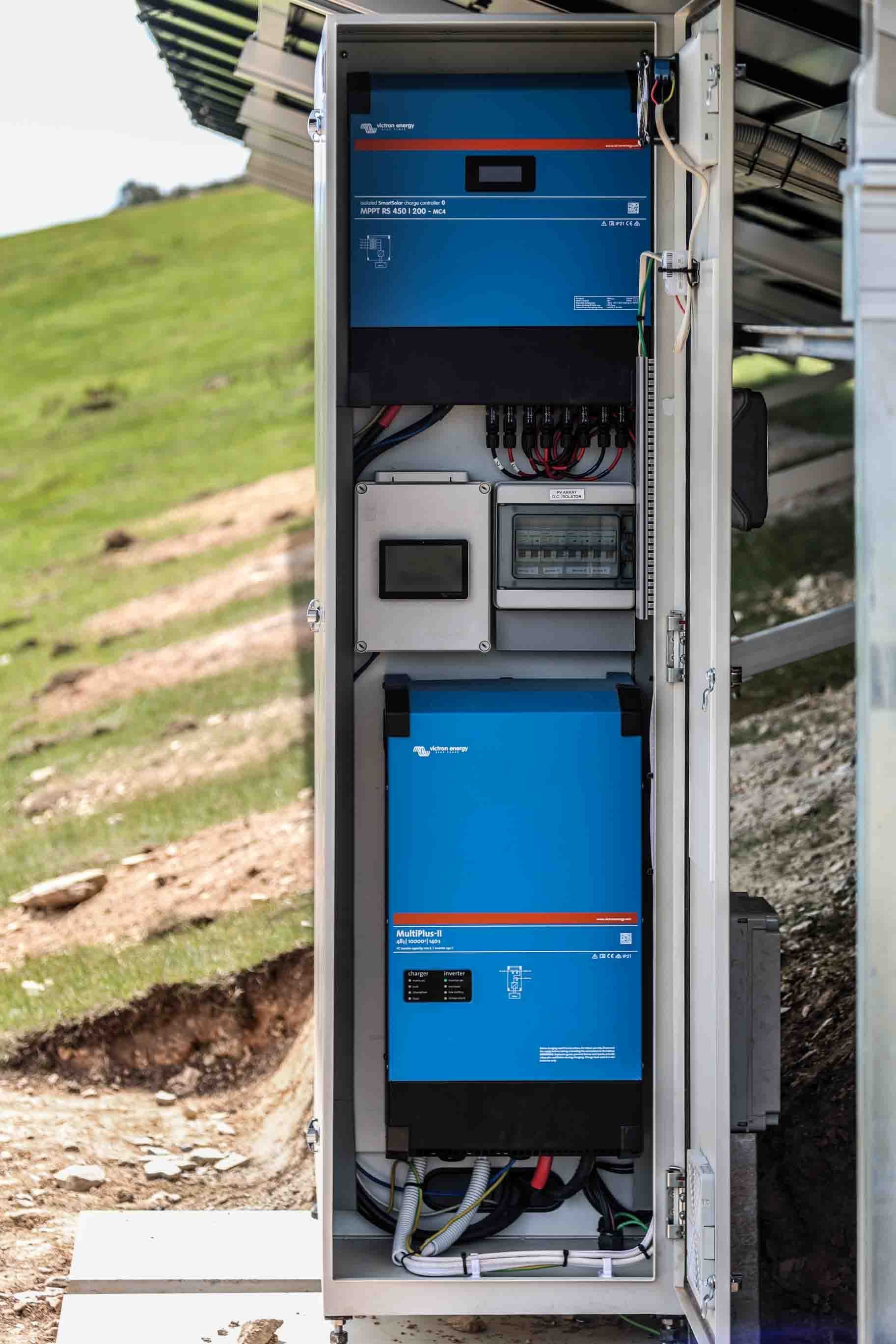 A Victron MultiPlus-II and MPPT RS in an outdoor cabinet beside a ground mounted array on a hillside